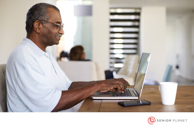 Photo of a black man in profile view using a laptop. He has short dark hair and glasses, and he is wearing a white t-shirt.