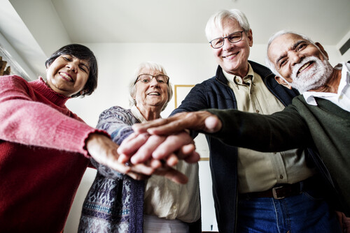 Photo shows four older adults stacking hands toward the front, center of the camera. 